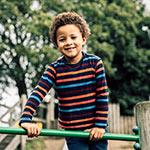 An image of a young boy smiling whilst on a climbing frame.