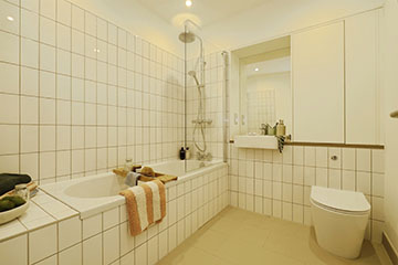 Burnholme Green internal bathroom photo showing a bath with overhead shower and shower screen, the bath is tiled to the sides under and over, the room is neutral in décor and also features a toilet, sink and mirror