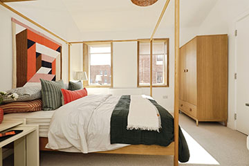 Burnholme Green internal bedroom photo showing a four poster bed, covered in bedding and pillows, looking very cosy, also in the room are some side tables and a large wardrobe. The décor is neutral and there a 2 large exterior windows on the far wall